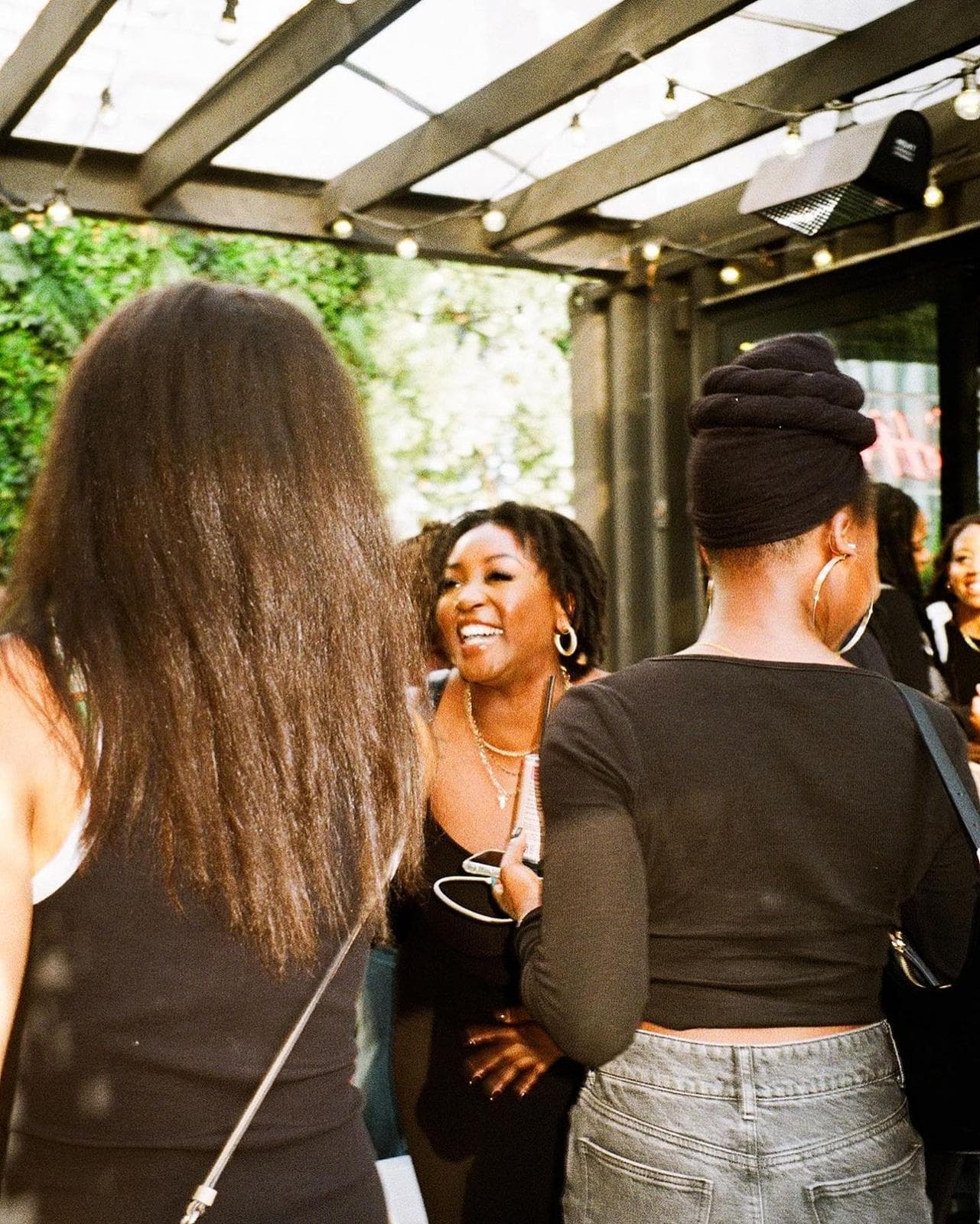 People socializing under a patio with string lights, focusing on two individuals' backs.