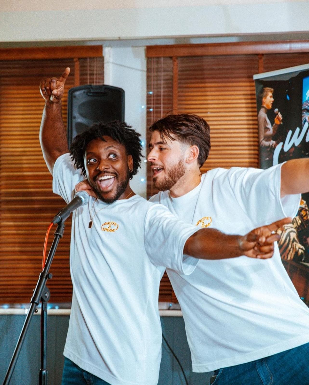Two people in white t-shirts dabbing on stage near a microphone.